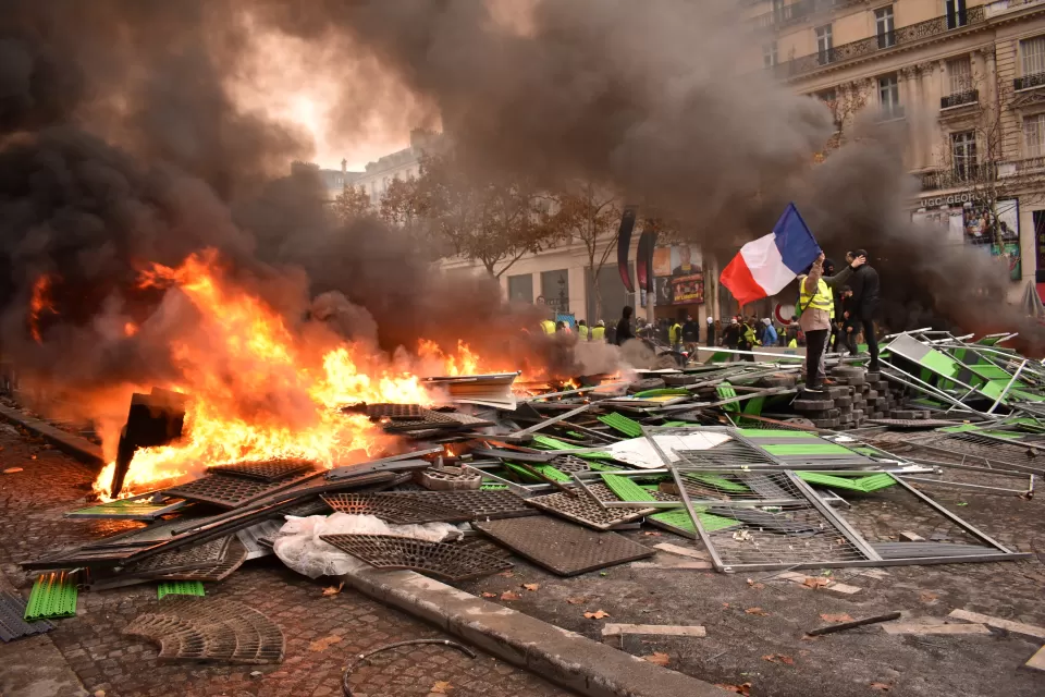 Person stands next to pile of burning debris in street holding French flag during Yellow Vest protests